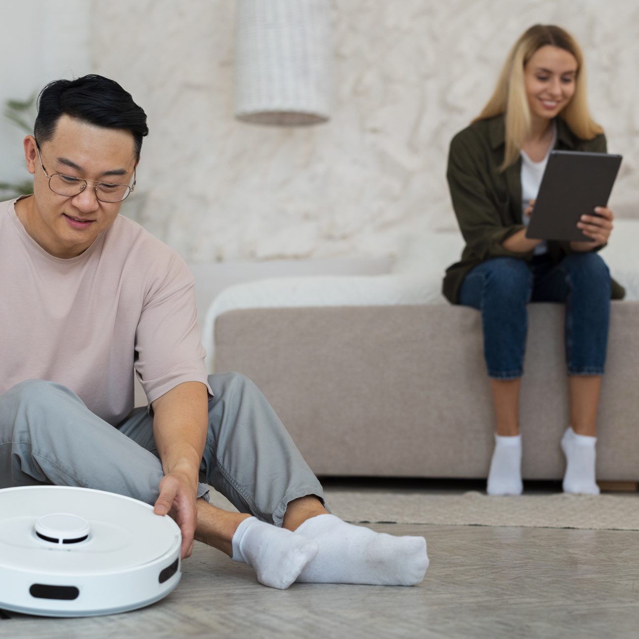 Man setting up a robot vacuum on floor while woman uses tablet on sofa in modern living room