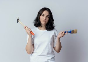 A woman holds two paintbrushes in one hand and a single paintbrush in the other, ready to create art
