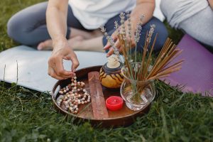 A woman on the grass examines a bowl of herbs and sticks, enjoying a moment in a natural outdoor setting